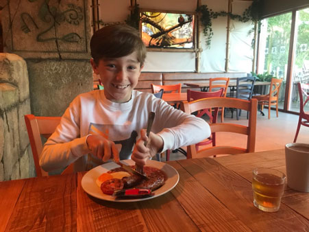 A young boy sitting at a table eating food
Description automatically generated